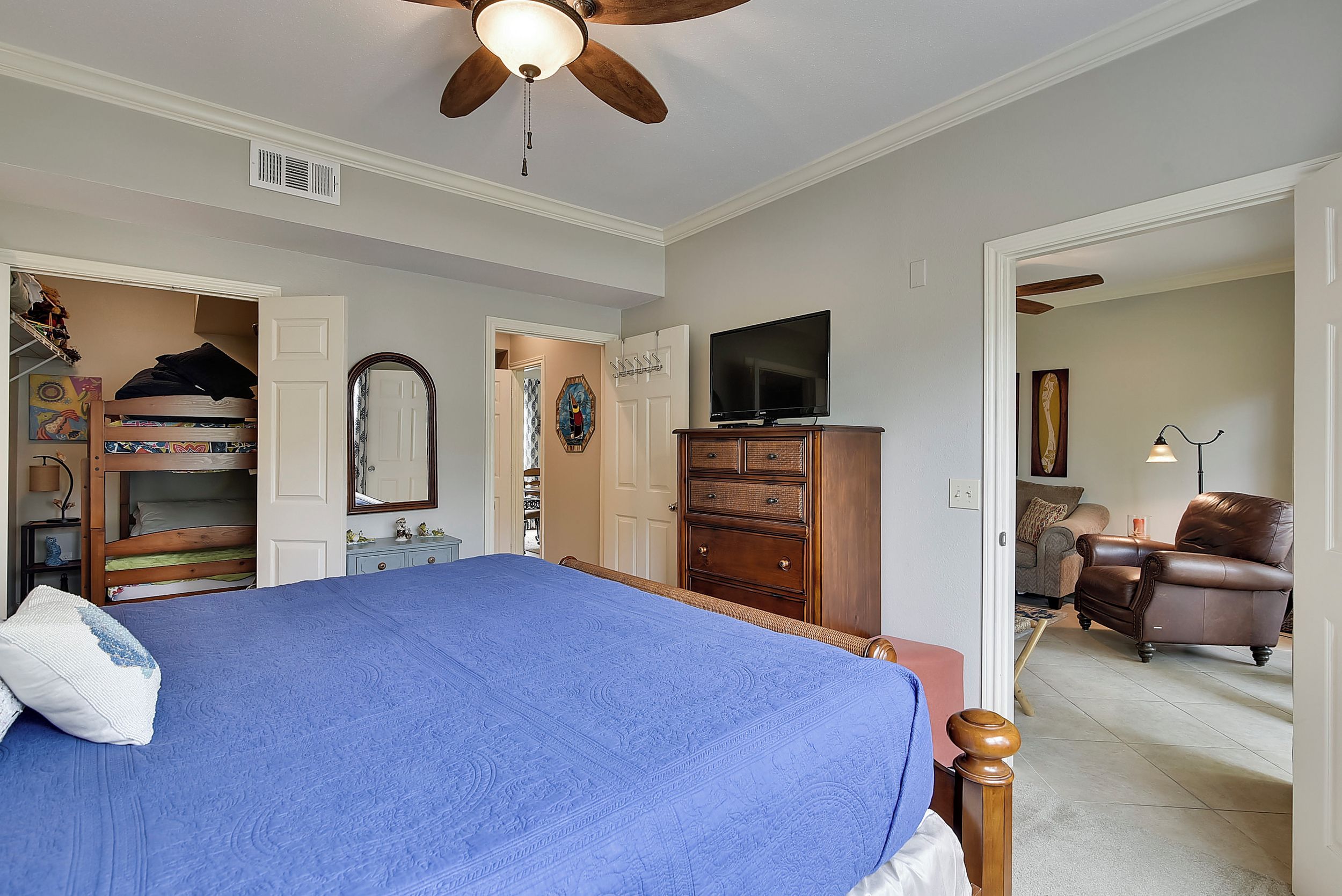 A bedroom with a bed, dresser, TV, and a ceiling fan.