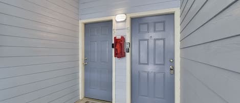 A hallway with two grey doors, a red mailbox, and a welcome mat.