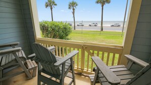 A porch with two Adirondack chairs and a view of the beach and parked cars. - Turtle Reef by Ryson Vacation Rentals (Galveston)