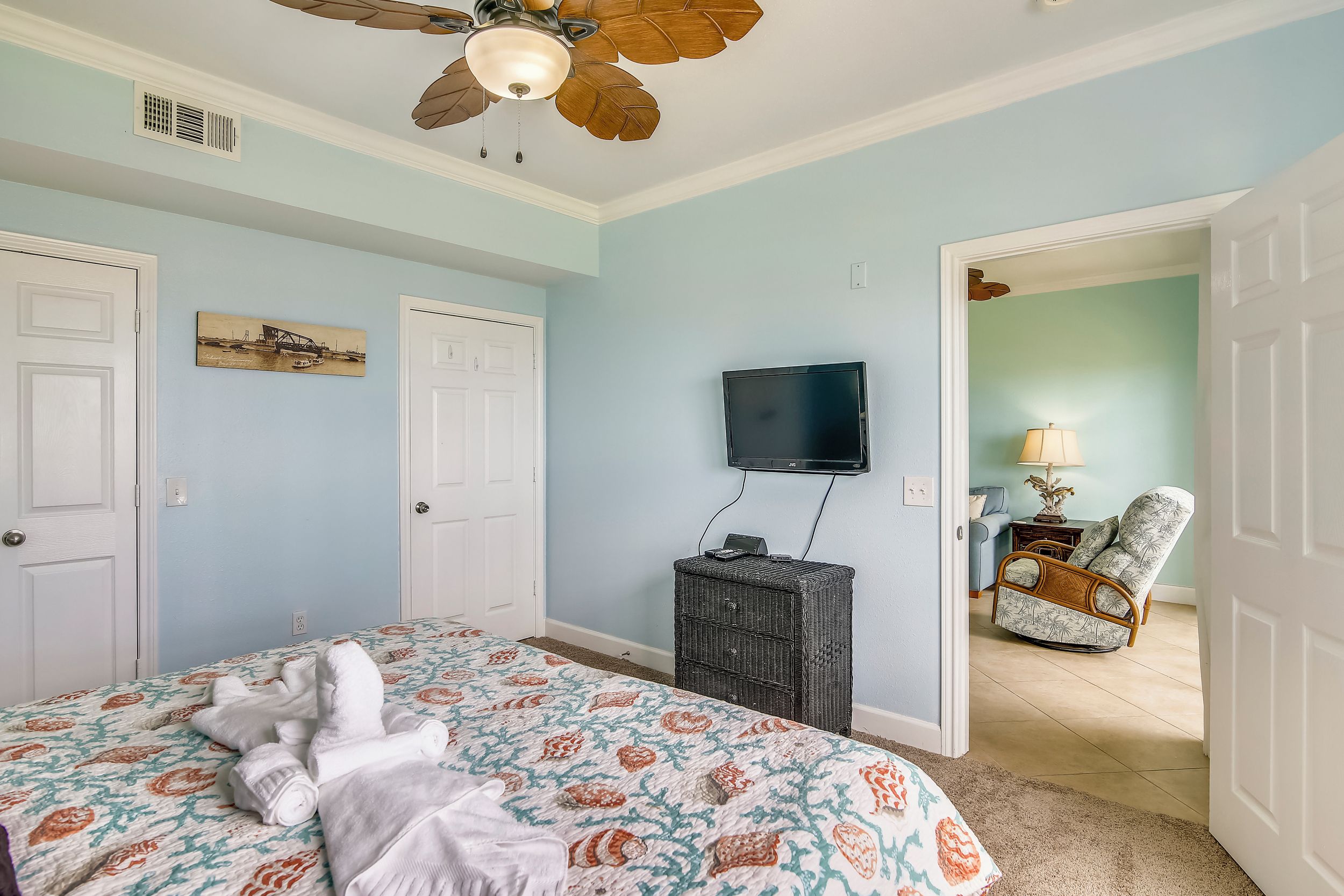 Une chambre à coucher comprenant un lit, un ventilateur de plafond, un téléviseur et une porte donnant sur une autre pièce.