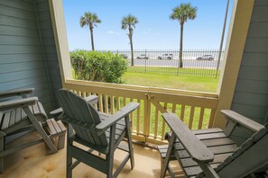 A porch with two Adirondack chairs and a view of the beach and parked cars. - Turtle Reef by Ryson Vacation Rentals (Galveston)