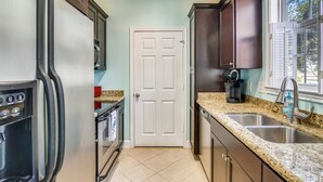 A kitchen with a stainless steel refrigerator, a double sink, and dark wooden cabinets. - Turtle Reef by Ryson Vacation Rentals (Galveston)