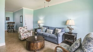 A living room with a blue sofa, patterned armchairs, a wooden coffee table, and a ceiling fan. - Turtle Reef by Ryson Vacation Rentals (Galveston)
