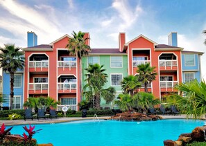 A hotel with colorful buildings, a swimming pool, and palm trees. - Turtle Reef by Ryson Vacation Rentals (Galveston)