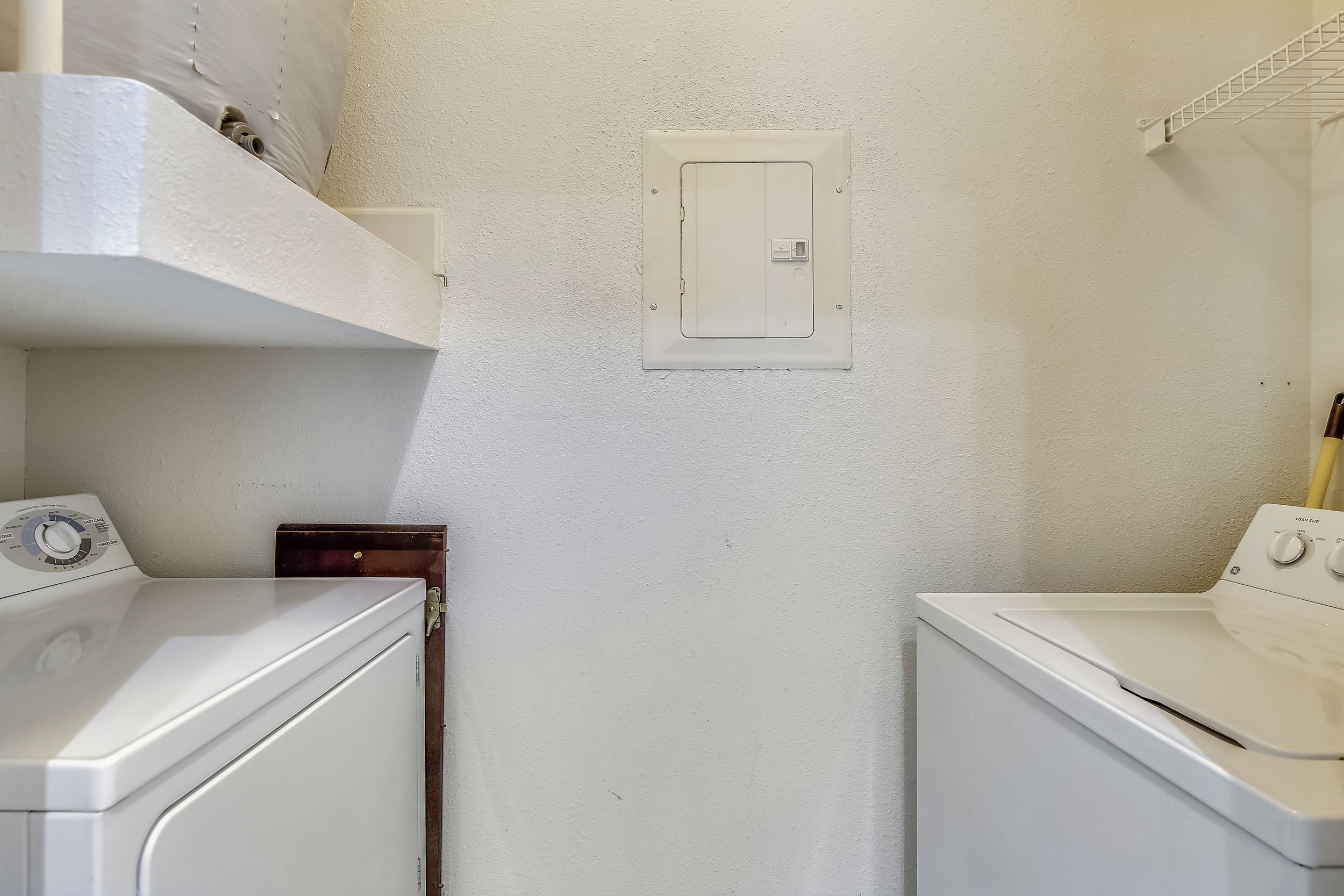 A laundry room with a washing machine, dryer, and a utility panel on the wall.