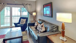 A living room with a leather sofa, a blue armchair, a coffee table, and a lamp. - Dawn 625 by Ryson Vacation Rentals (Galveston)