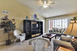 A living room with a ceiling fan, a large window, a sofa, a chair, and a bookshelf. - Dawn 631 by Ryson Vacation Rentals (Galveston)