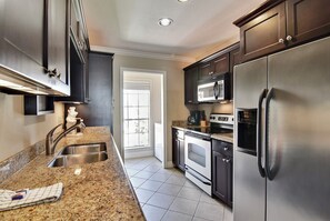 A modern kitchen with stainless steel appliances, granite countertops, and dark cabinetry. - Dawn 631 by Ryson Vacation Rentals (Galveston)