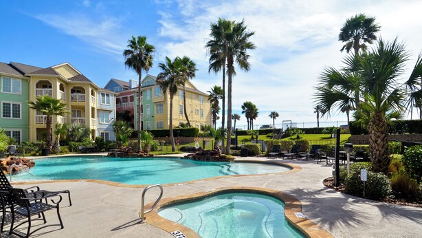 A swimming pool area with multiple pools, lounge chairs, and palm trees. - Dawn 631 by Ryson Vacation Rentals (Galveston)