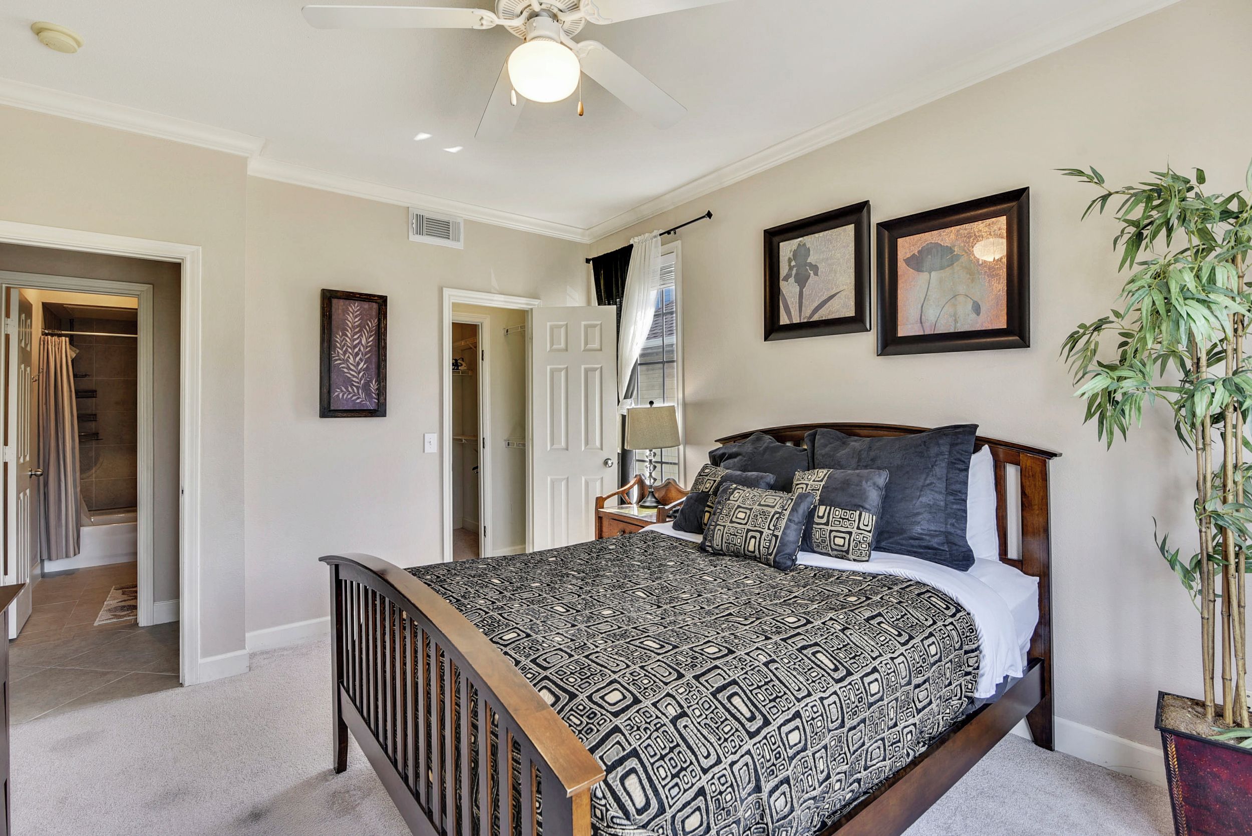 A bedroom with a large bed, a ceiling fan, and two framed artworks on the wall.