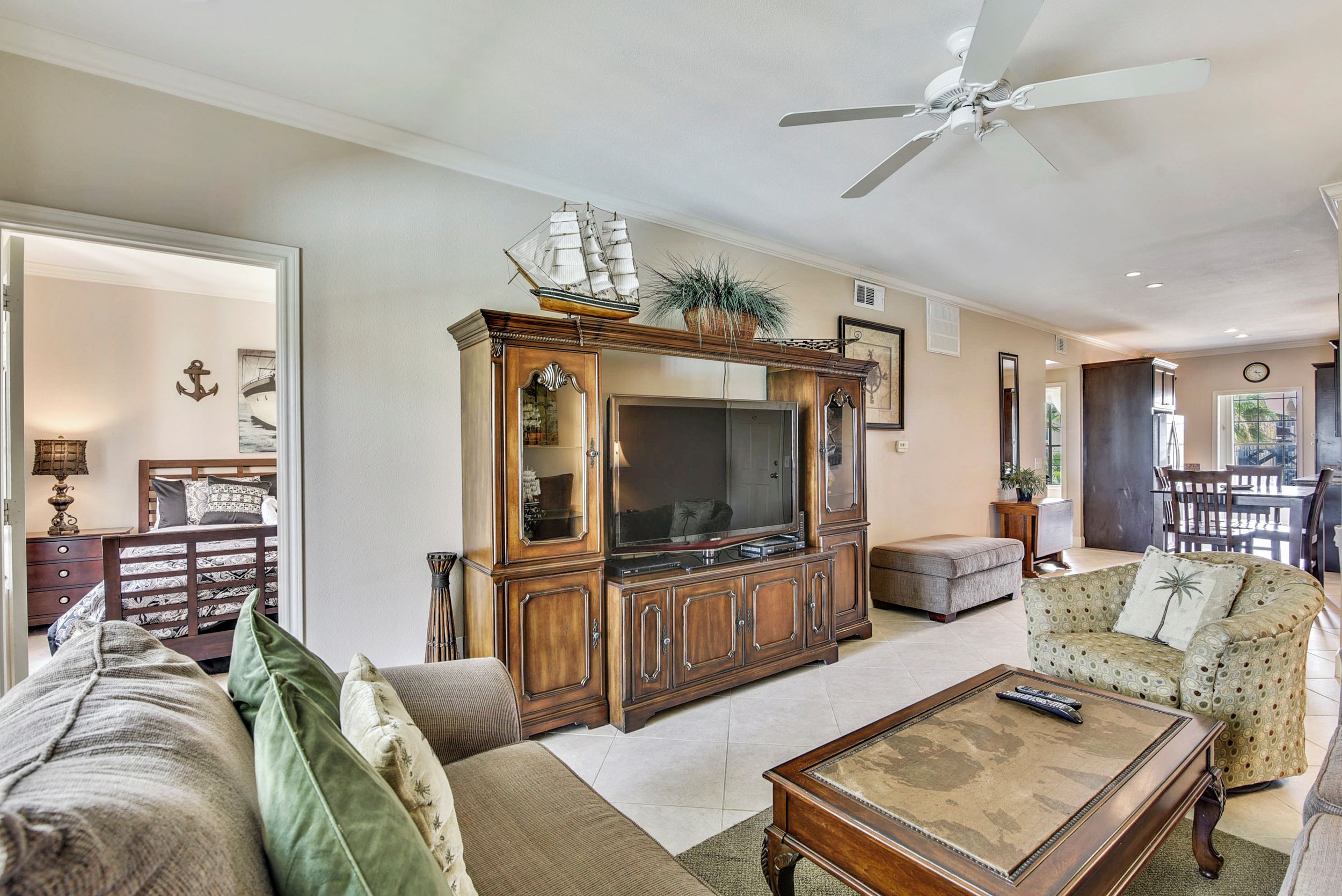 A living room with a large TV, wooden entertainment center, and a ceiling fan.