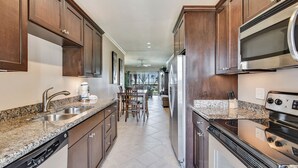 A modern kitchen with granite countertops, stainless steel appliances, and wooden cabinets. - Sea n' Swim by Ryson Vacation Rentals (Galveston)