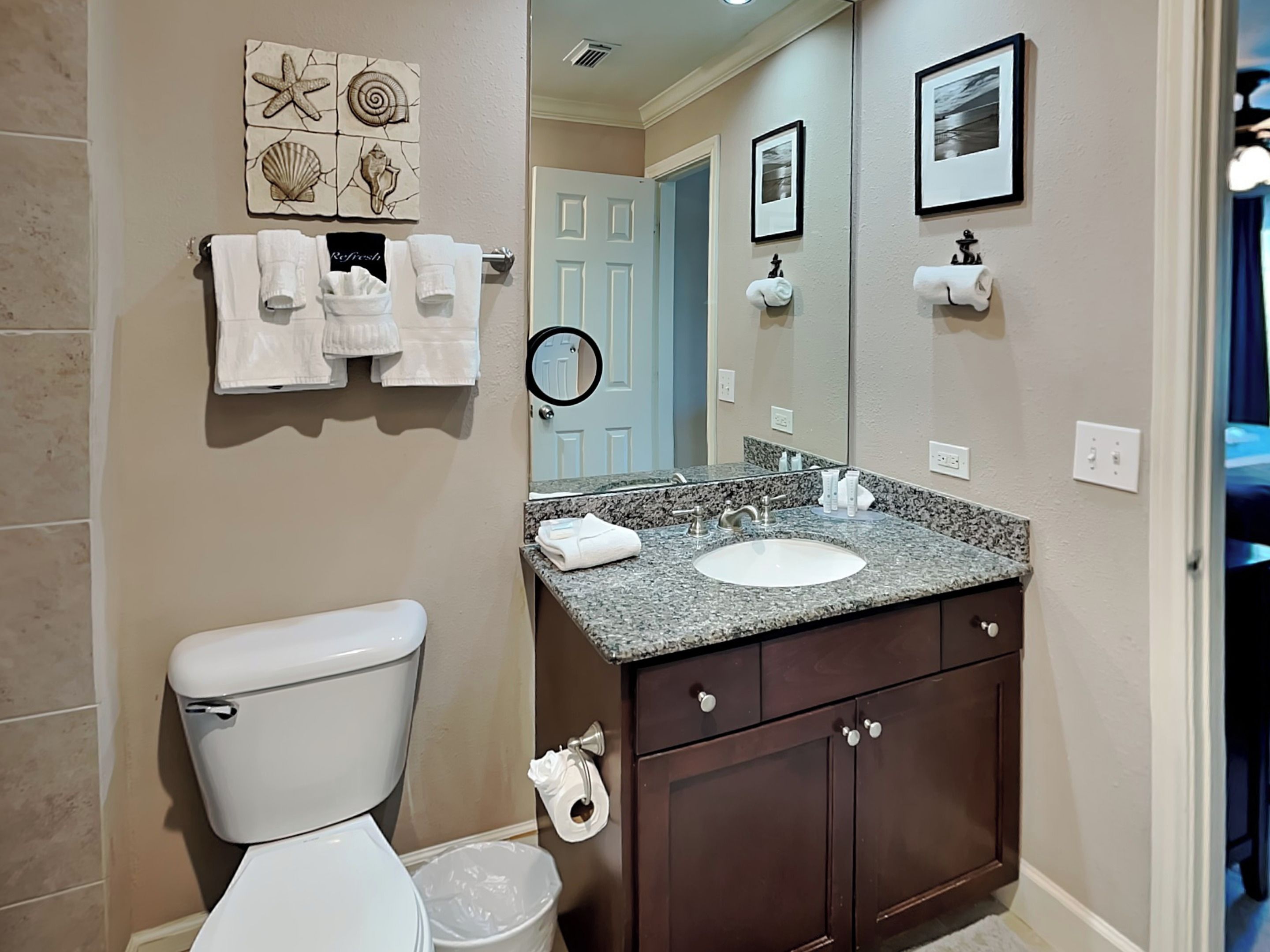 A bathroom with a toilet, sink, and vanity. There are towels hanging on a rack, a trash can, and a mirror above the sink.