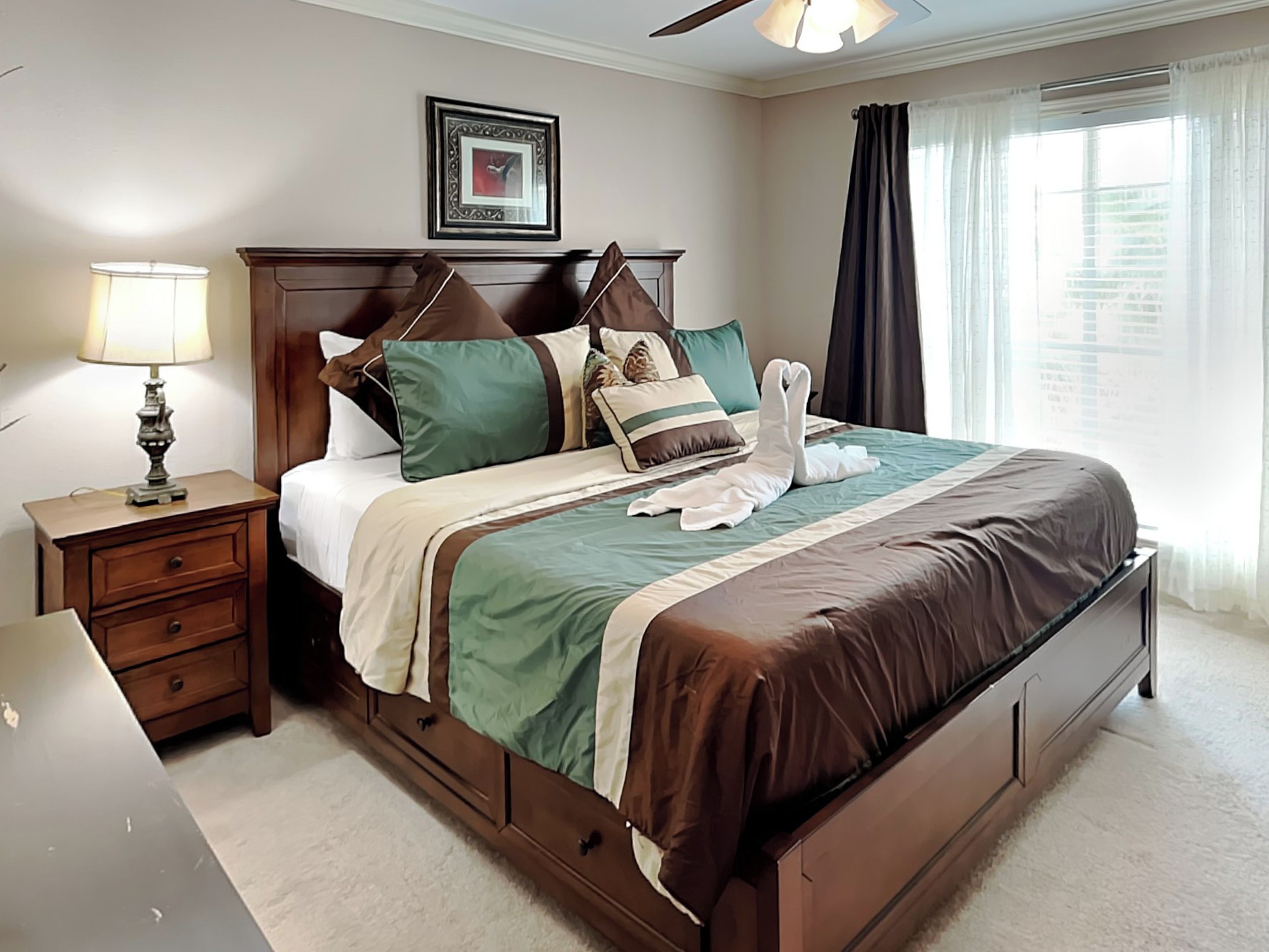 A neatly made bed with a brown headboard, a bedside table with a lamp, and a framed picture on the wall.