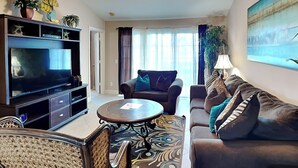 A living room with a TV, sofa, chairs, a ceiling fan, and a painting. - Just for Fun by Ryson Vacation Rentals (Galveston)