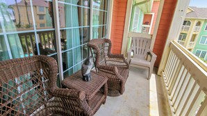 A balcony with wicker furniture and a plastic chair, overlooking a residential area. - Just for Fun by Ryson Vacation Rentals (Galveston)