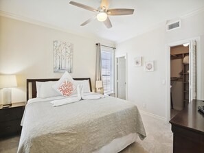 Cozy retreat with a large bed, ceiling fan, and large window with blinds.
