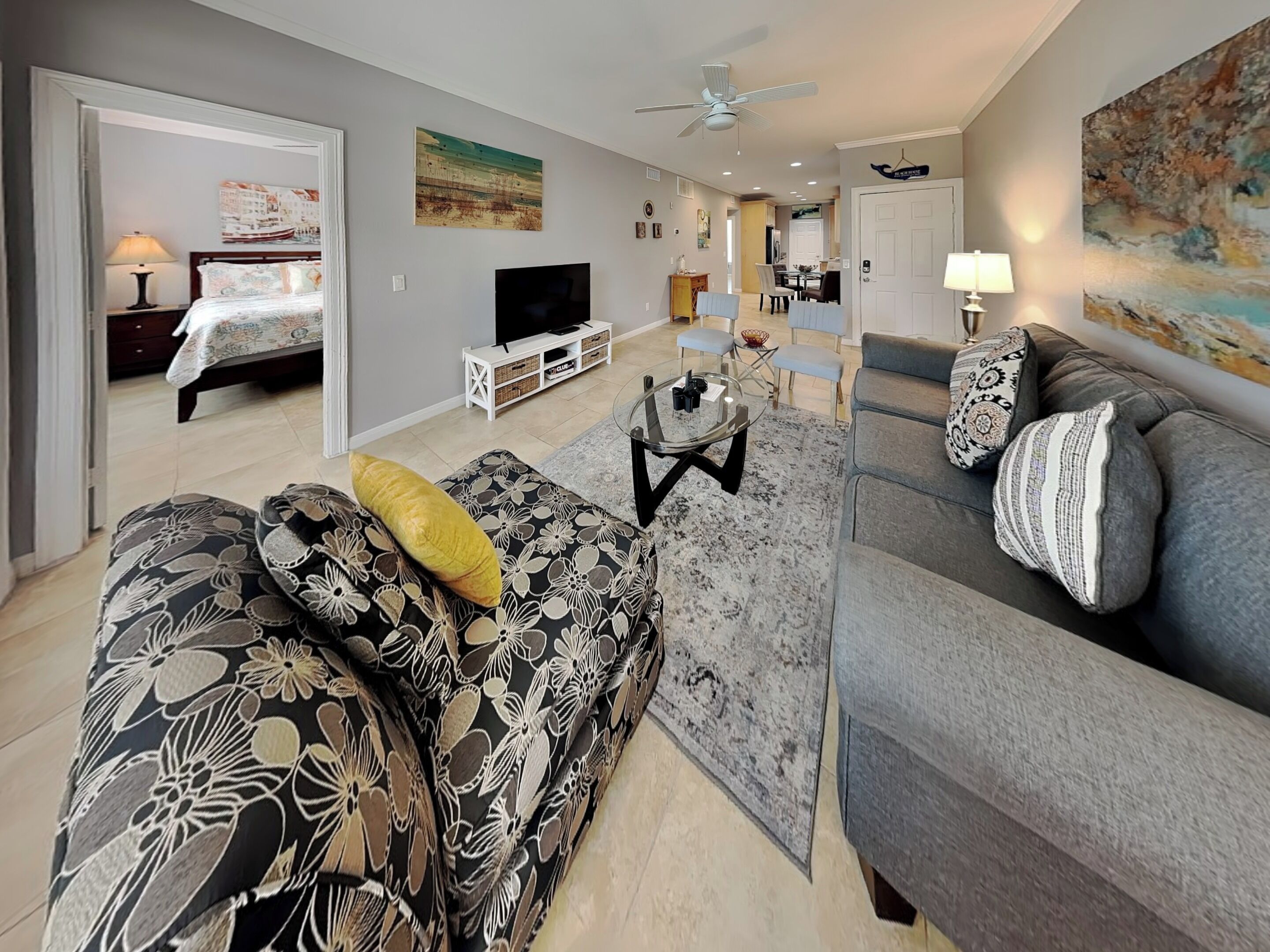 A living room with a sofa, a television, a dining area, and a hallway.