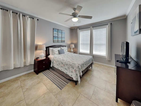 A bedroom with a bed, nightstands, a desk, a ceiling fan, and a window with blinds.