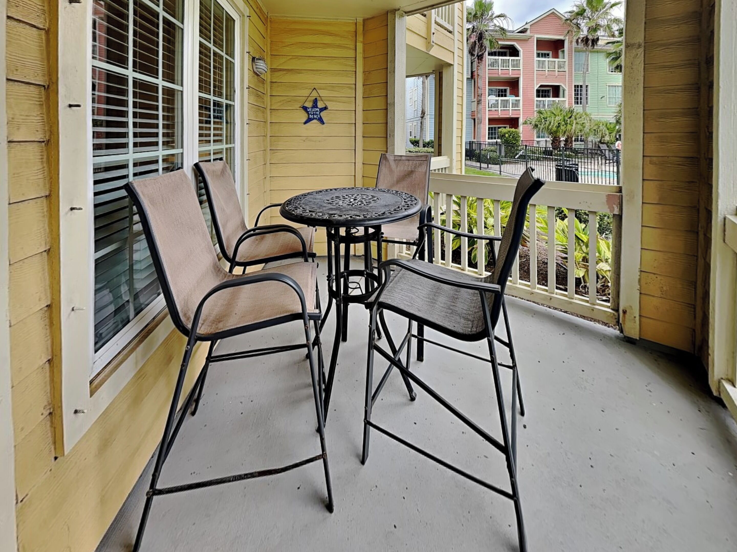 Een balkon met een tafel en stoelen, een decoratief bord en uitzicht op kleurrijke gebouwen op de achtergrond.