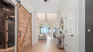 A hallway with a wooden sliding door, a white wall, and a view to a living area with a sofa and a window. - Big Canoe Mountain Home with Spectacular Mountain Views - Game room! (Jasper)