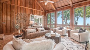 A spacious living room with a high ceiling, wooden walls, and large windows offering a view of trees. - Big Canoe Mountain Home with Spectacular Mountain Views - Game room! (Jasper)