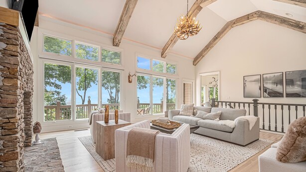 A spacious living room with a stone fireplace, large windows, a gray sofa, and a chandelier. - Big Canoe Mountain Home with Spectacular Mountain Views - Game room! (Jasper)