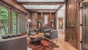 A spacious living room with leather sofas, a round coffee table, and a large window offering a view of trees. - Big Canoe Mountain Home with Spectacular Mountain Views - Game room! (Jasper)