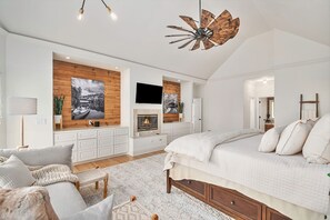 Une chambre spacieuse avec un grand lit, une cheminée, des boiseries et un ventilateur de plafond.