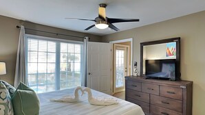 Ein Hotelzimmer mit Bett, Fernseher, Deckenventilator, Kommode und Balkontür.