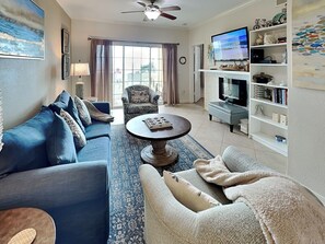 A living room with a blue sofa, a patterned armchair, a coffee table, and a TV on a stand.