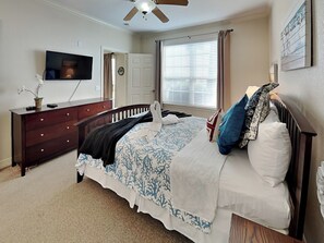 Quarto com cama, cómoda, televisão e janela com persianas.