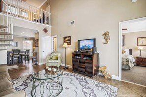 Un salon spacieux avec un escalier, un téléviseur et un coin repas.