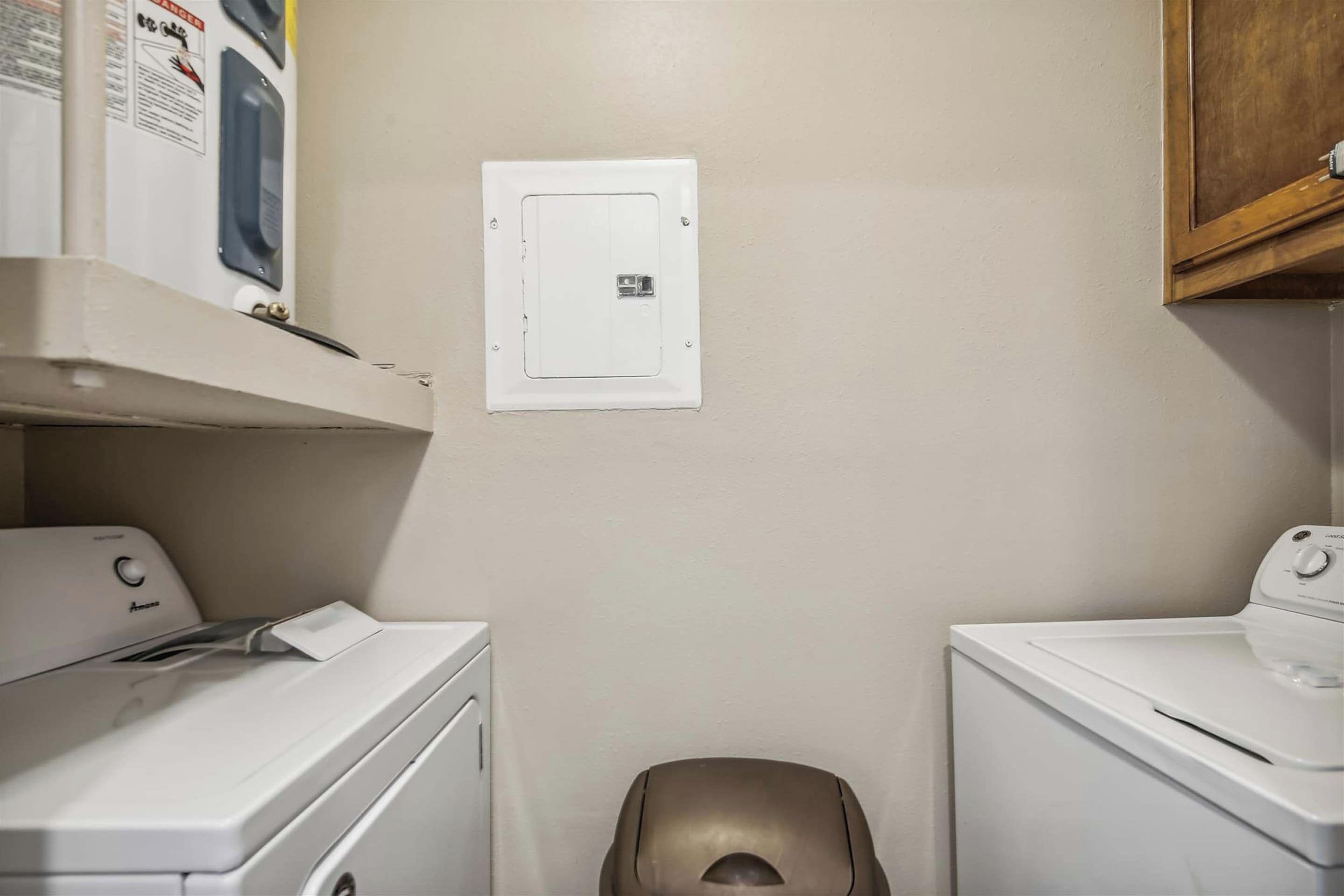 A laundry area with two washing machines, a dryer, and a utility panel on the wall.