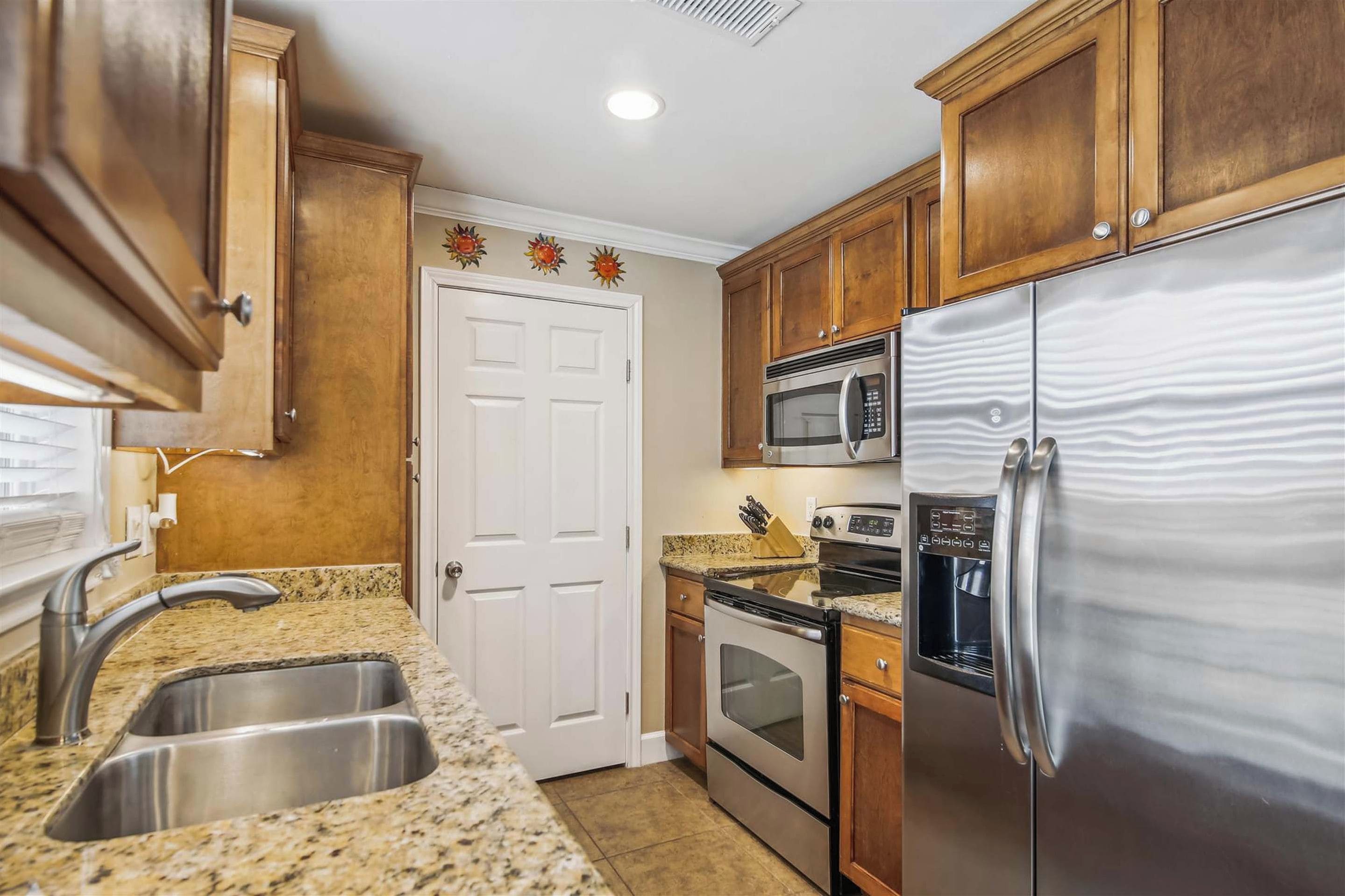 A kitchen with granite countertops, stainless steel appliances, wooden cabinets, and a white door.