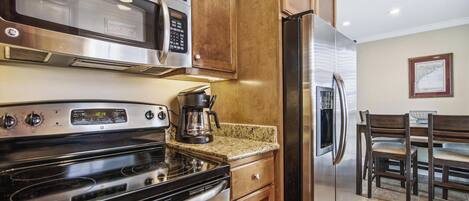 A kitchen with stainless steel appliances, wooden cabinets, a granite countertop, and a dining area with a table and chairs.