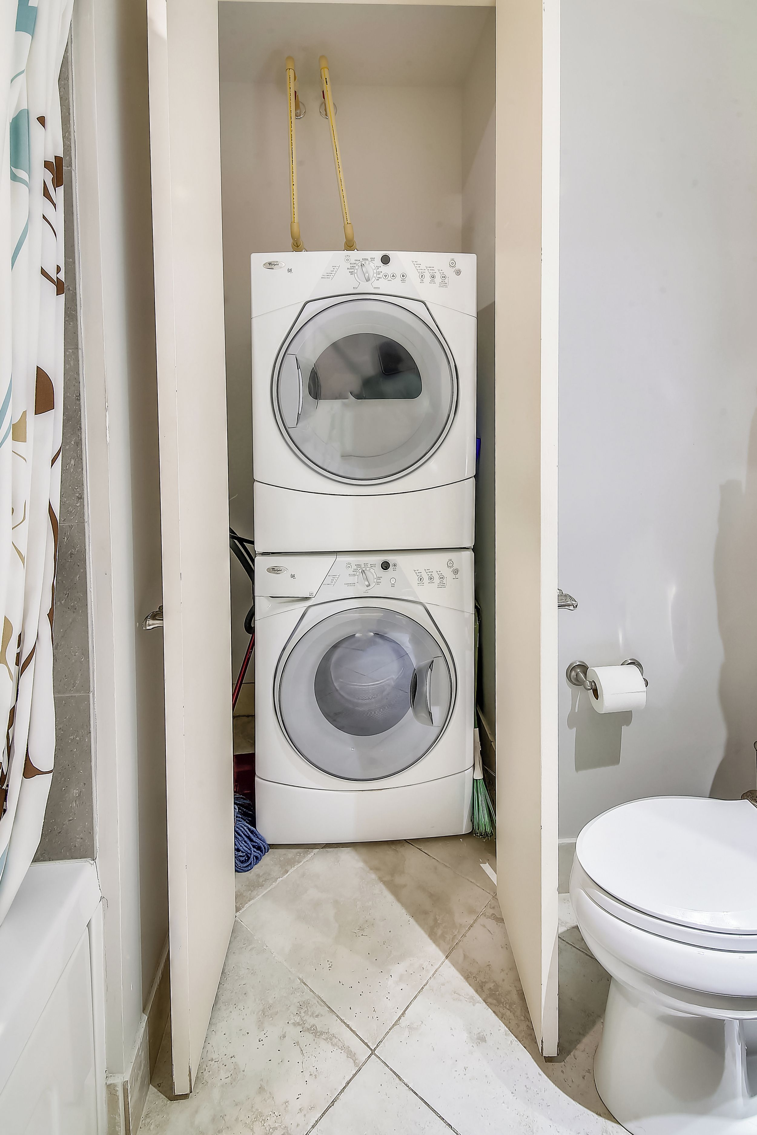 Een wasserette met twee gestapelde wasmachines, een toilet en een douchegordijn.