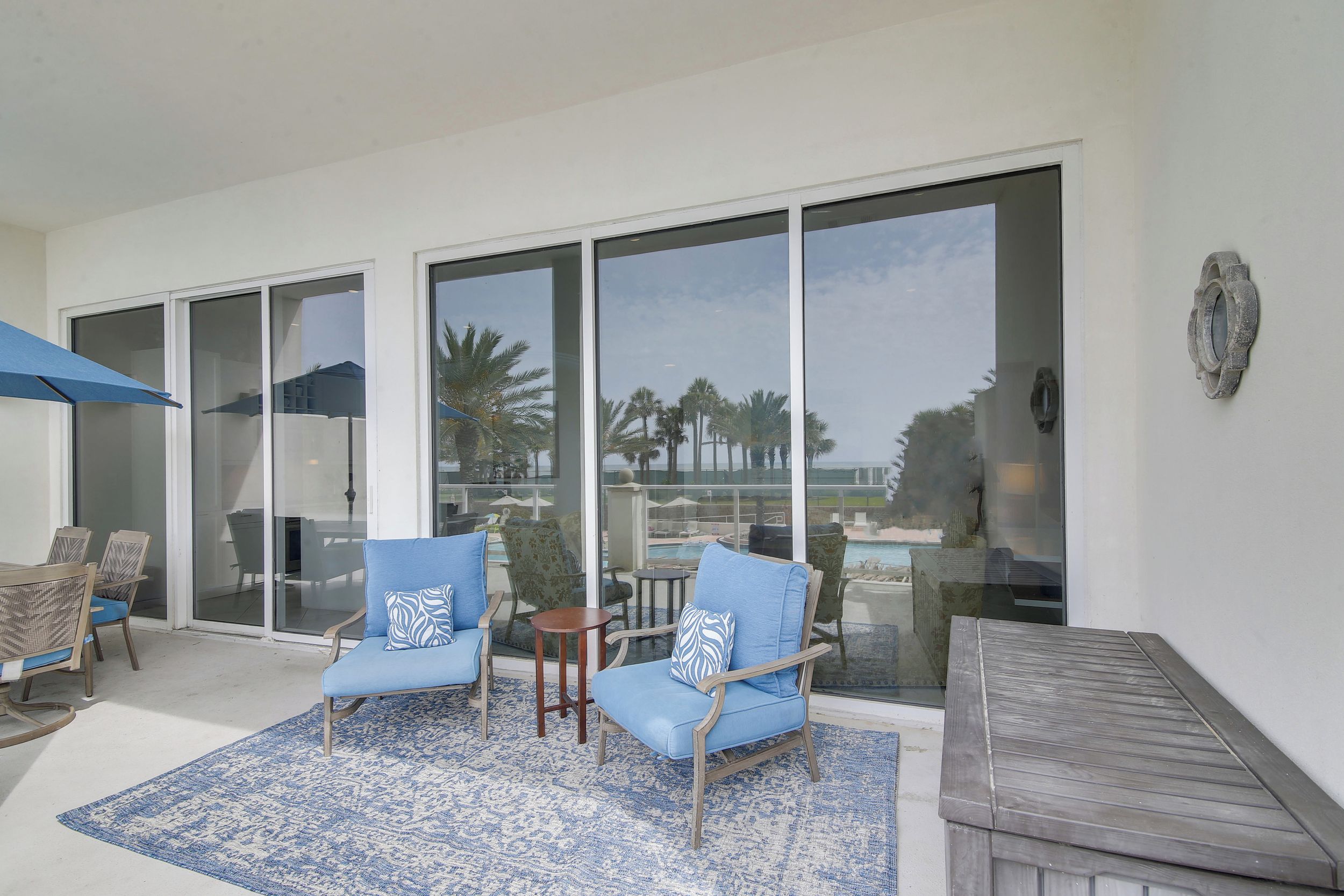 A modern outdoor seating area with two blue cushioned chairs, a small round table, and a blue patterned rug.
