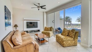 A spacious living room with a large TV, comfortable seating, and a balcony with a view. - Beach Time by Ryson Vacation Rentals (Galveston)
