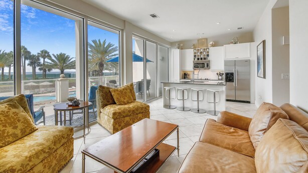 A spacious living area with a large window, a kitchen, and a pool view. - Beach Time by Ryson Vacation Rentals (Galveston)