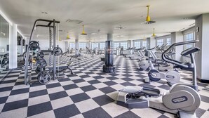Une salle de sport avec un sol à carreaux, divers appareils d’exercice et de grandes fenêtres.