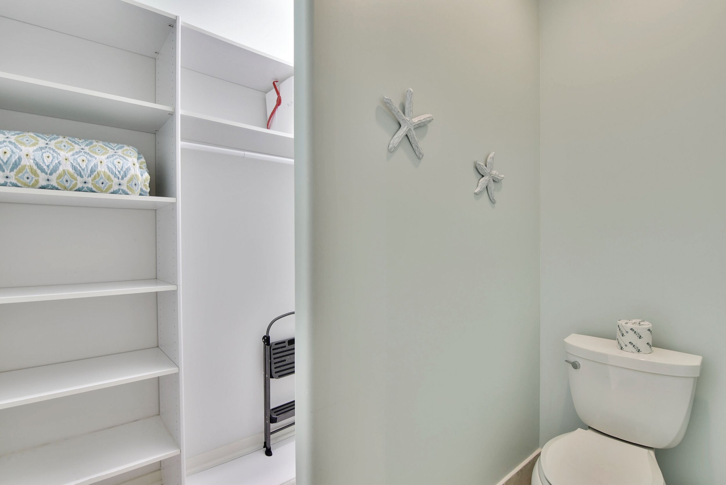 A bathroom with a toilet, a shelf with a patterned item, and decorative wall art.