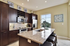 A modern kitchen with dark wood cabinets, stainless steel appliances, and a granite countertop island with bar stools. - Sapphire by Ryson Vacation Rentals (Galveston)