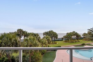 A pool area with a view of the ocean, surrounded by palm trees and a well-maintained lawn.