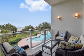 A balcony with wicker furniture, a view of a pool, and a clear sky.