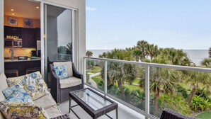 Ein Balkon mit Glastisch und Korbmöbeln, der Blick auf einen Strand und Palmen freigibt.