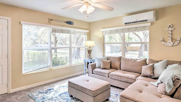 A living room with a beige sofa, an ottoman, a ceiling fan, and large windows with blinds. - < 1 Mi to Lake Weir: Quiet Summerfield Getaway (Summerfield)