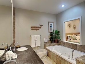Une salle de bain moderne avec une grande baignoire, deux lavabos, un miroir, une plante en pot et un tableau encadré au mur.
