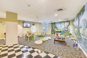 Un espace de jeux pour enfants avec un sol à carreaux, des sièges verts et une fresque représentant des animaux.