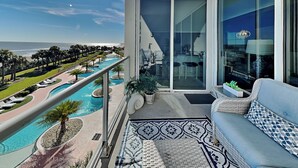Un balcone con vista su una piscina e l'oceano, un divano e un'area pranzo.
